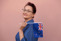 New Zealand flag. Woman holding the flag of New Zealand. Nice portrait of middle aged lady 40 50 years old with a national flag over pink wall background.