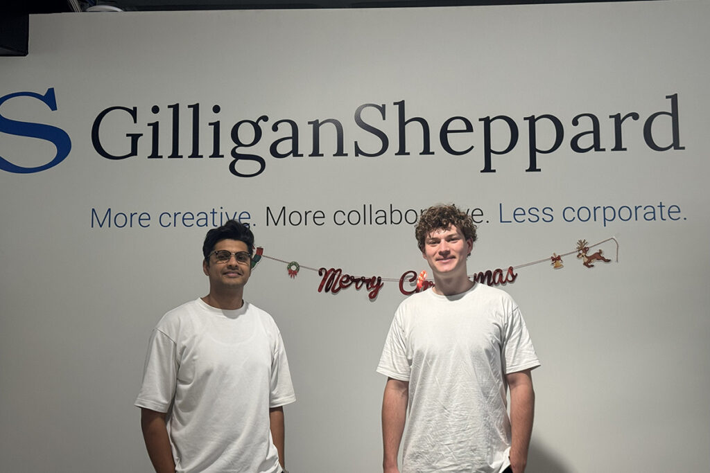 Sahil and Toby standing in front of Gilligan Sheppard sign