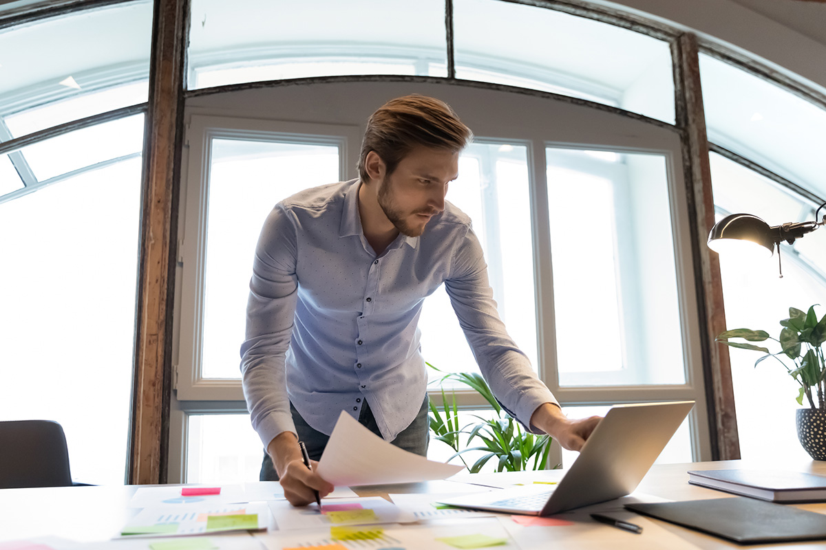 Business man comparing data on paper and laptop