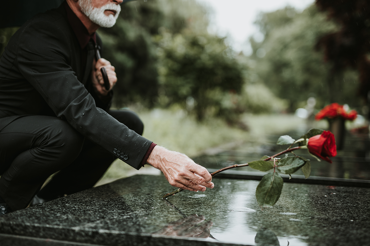old man laying rose on stone grave