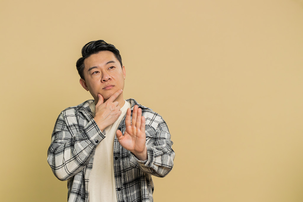 asian man pondering with hand raised in a 'stop' position