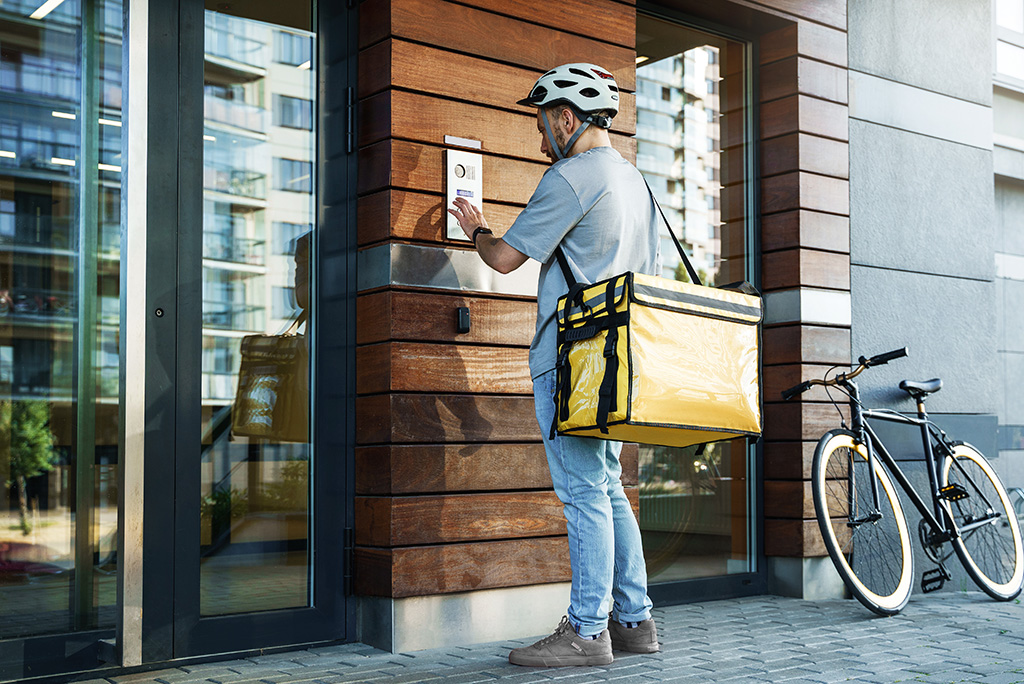 food delivery man with insulated bag pressing intercom to apartment building