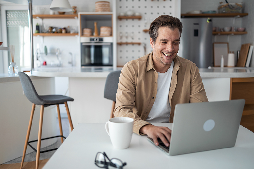Smiling middle-aged man looks pleased as he answers emails from his laptop from the comfort of his home.