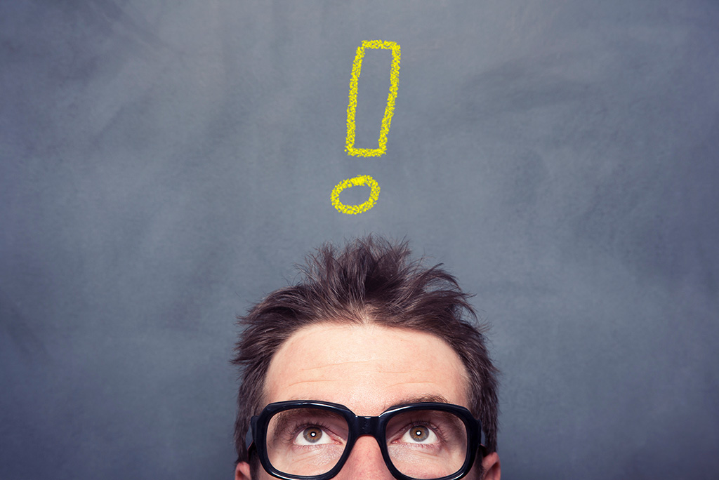 man wearing glasses standing under yellow chalk exclamation point
