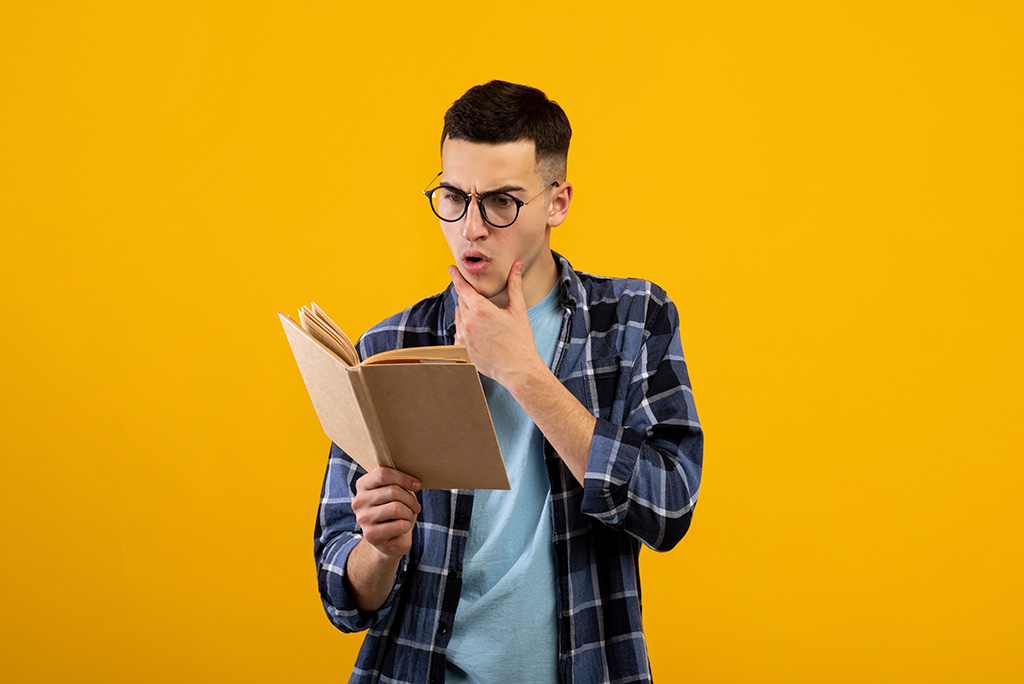 man reading a book with intrigued facial expression