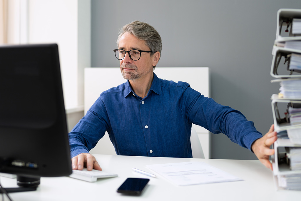 businessman working on computer pushing away binders