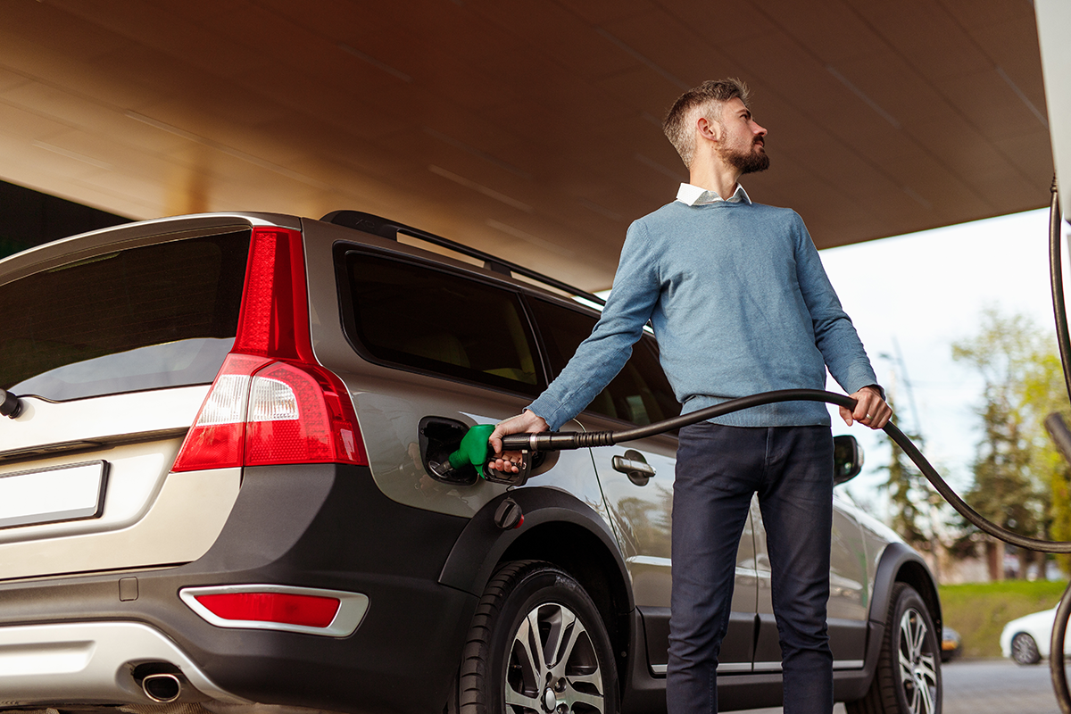 Man checking fuel pump prices while filling car with petrol