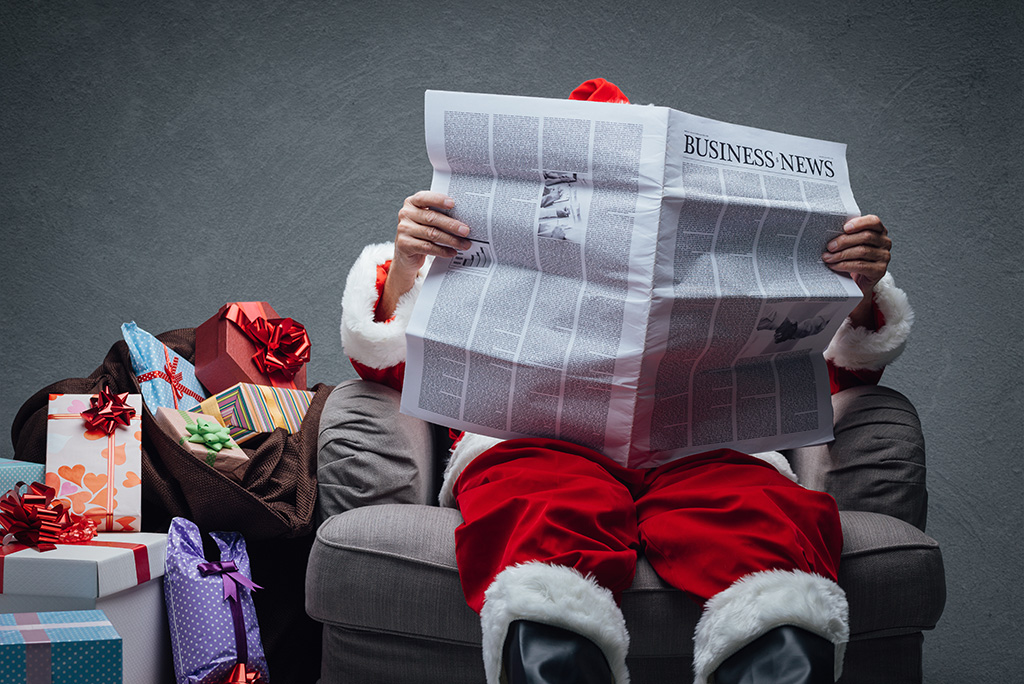 Santa reading business newspaper on armchair next to sack of gifts