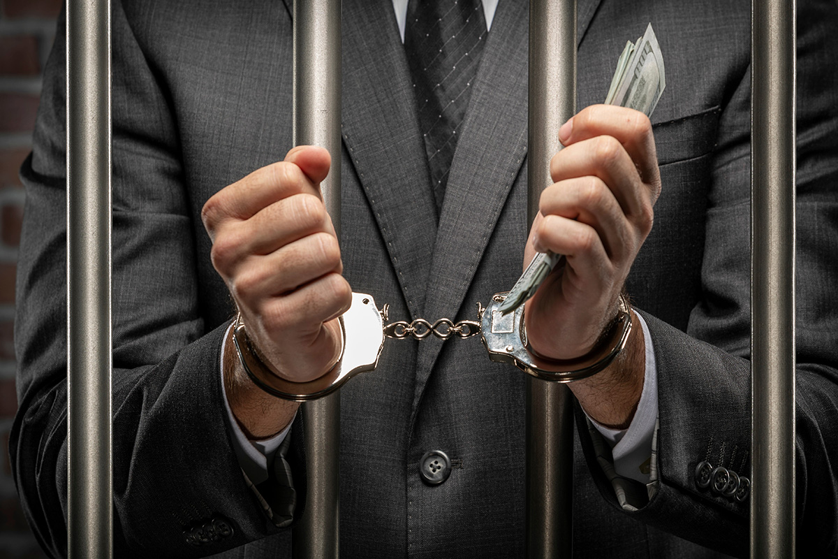 business man holding money behind bars and in handcuffs